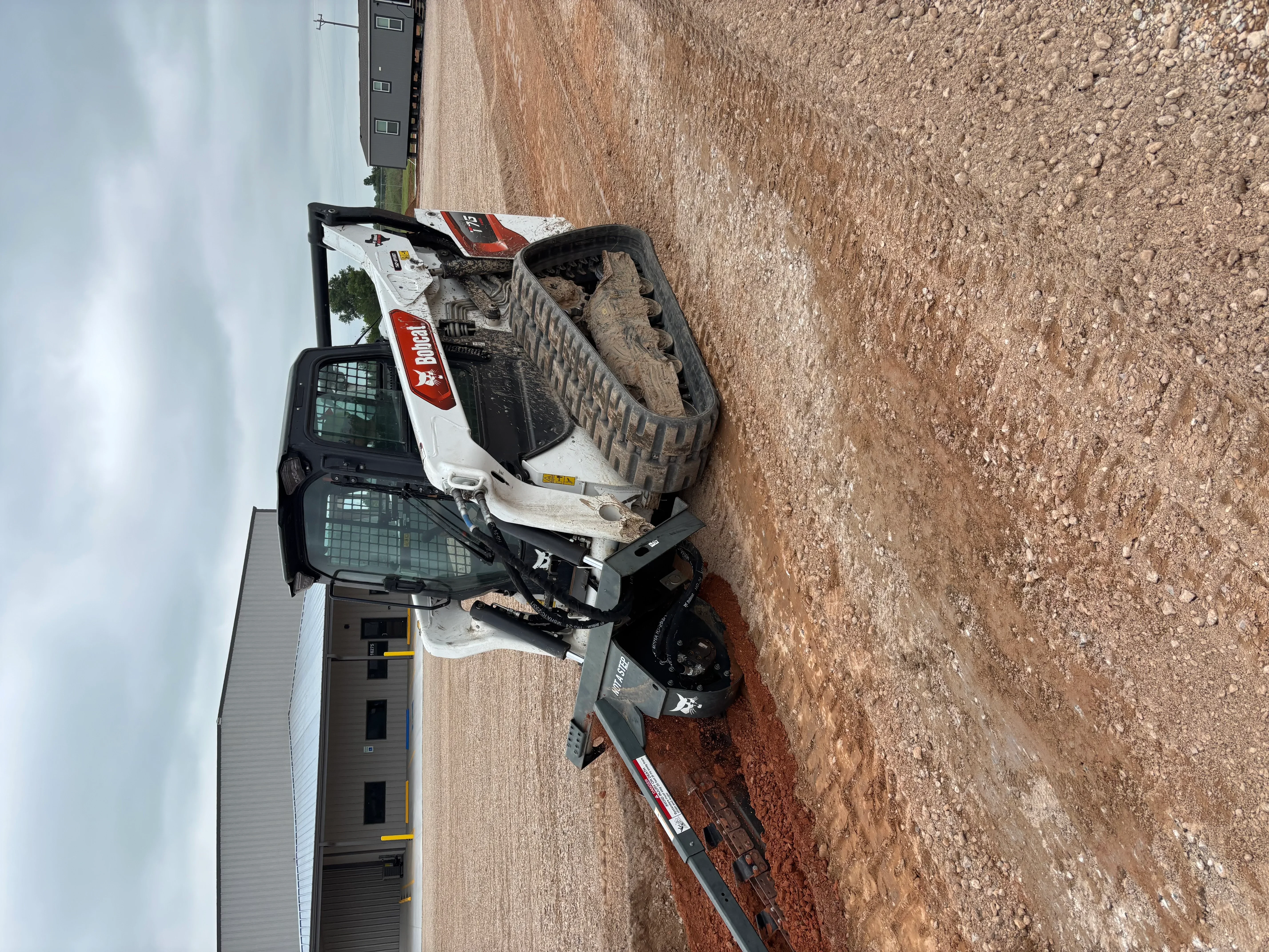 Skid steer loader excavating and grading soil on residential construction site