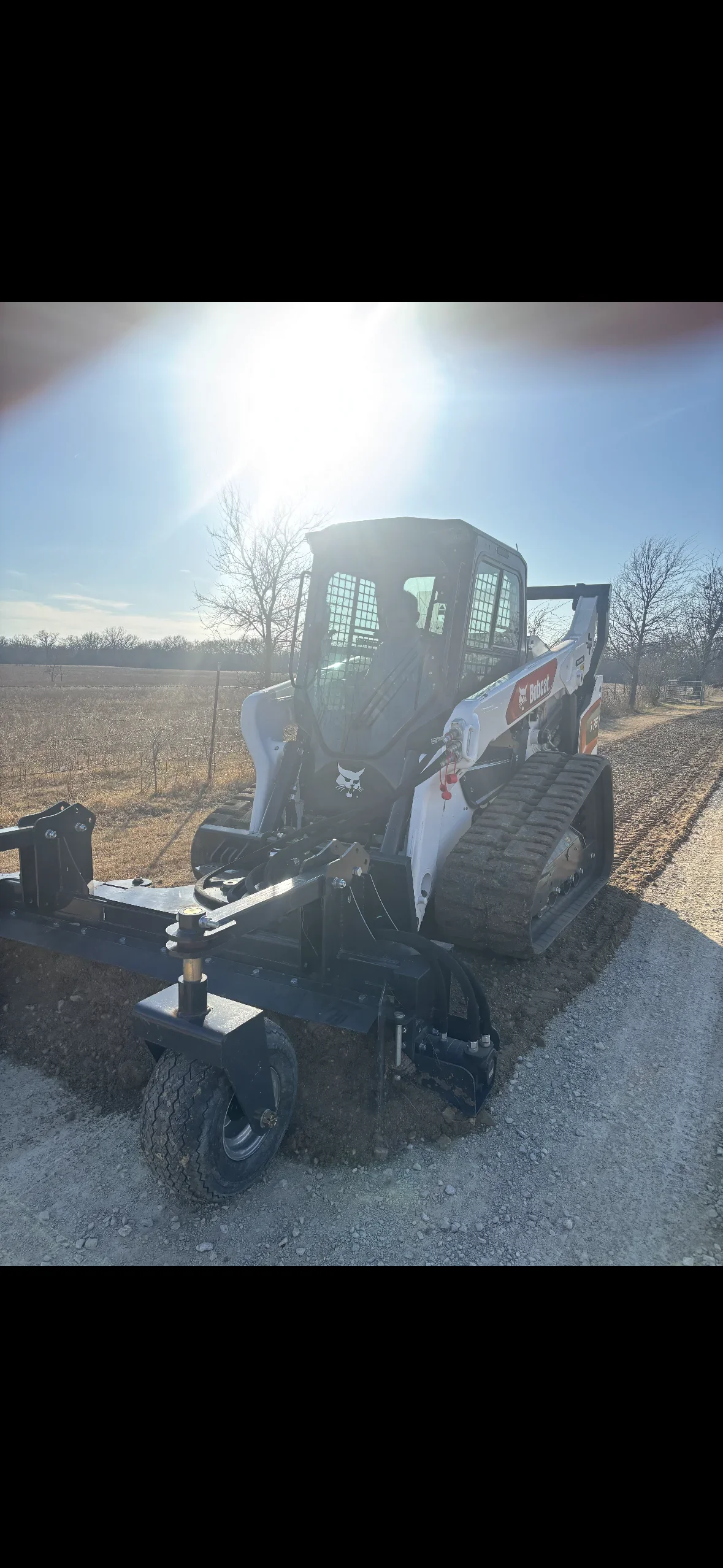 Compact track loader with grading blade on rural driveway site