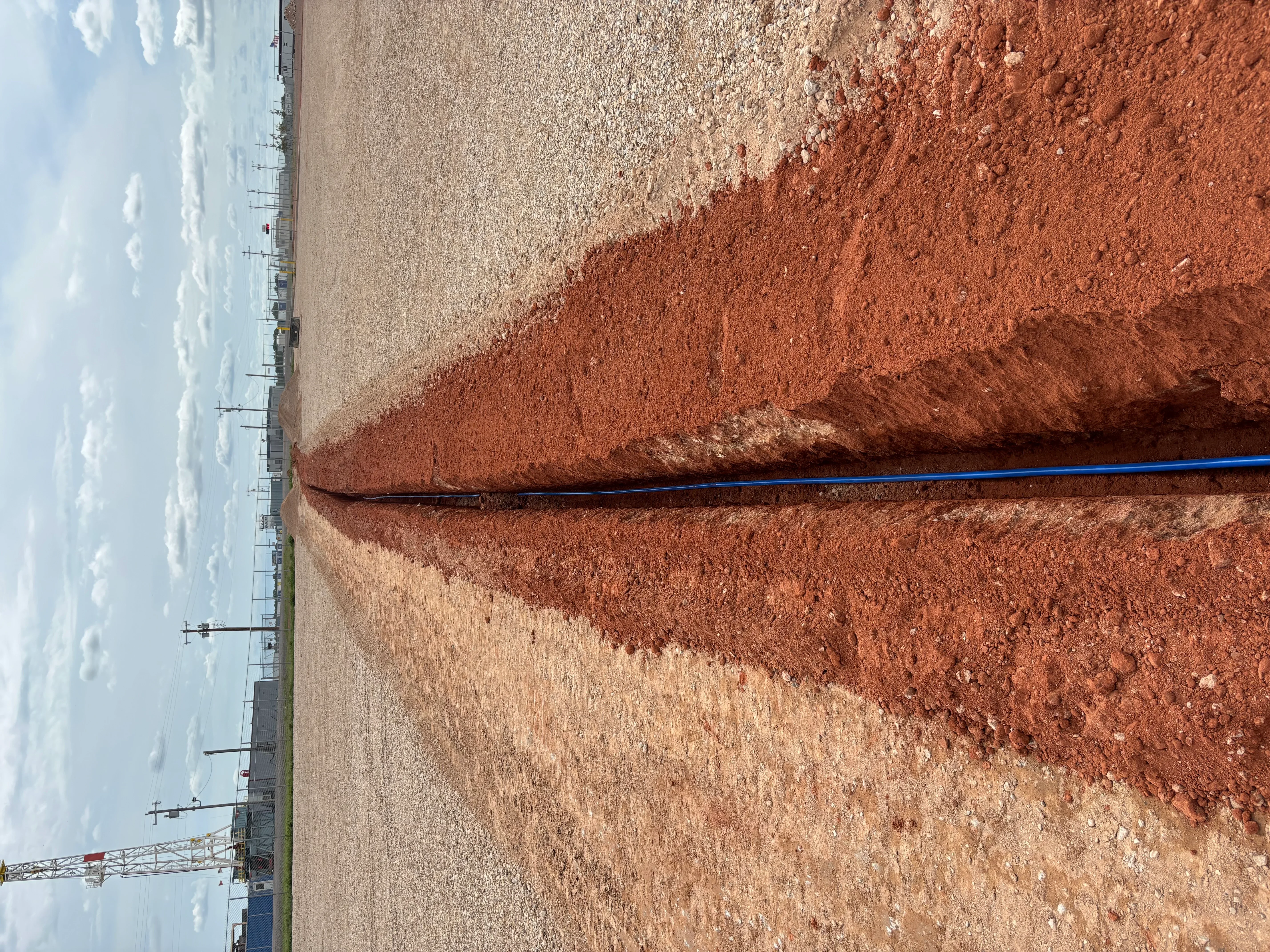 Excavated and graded site with layered soil and blue PVC drainage pipe installation