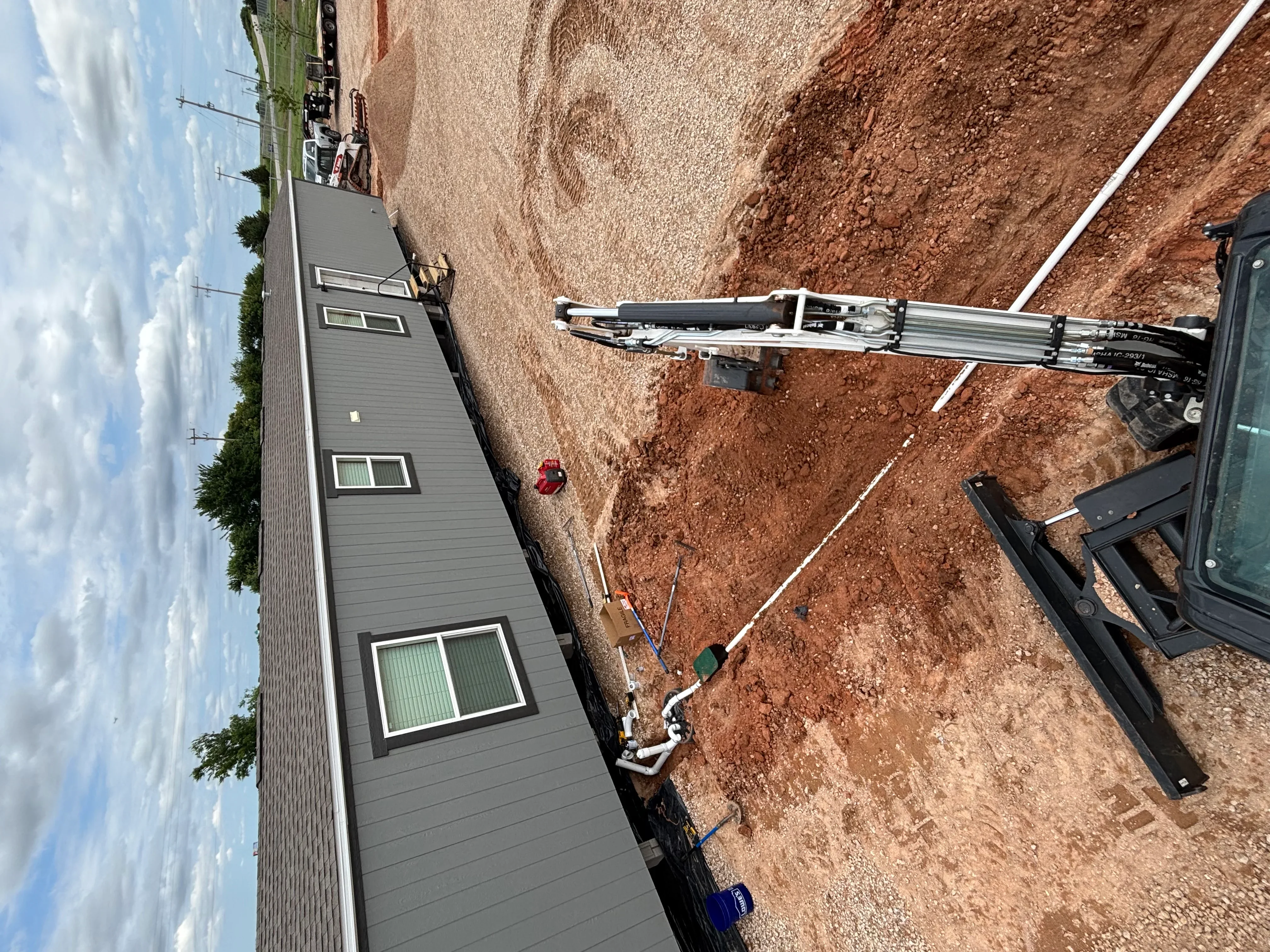 Foundation installation with white PVC drainage pipe, excavated site, and new residential home structure