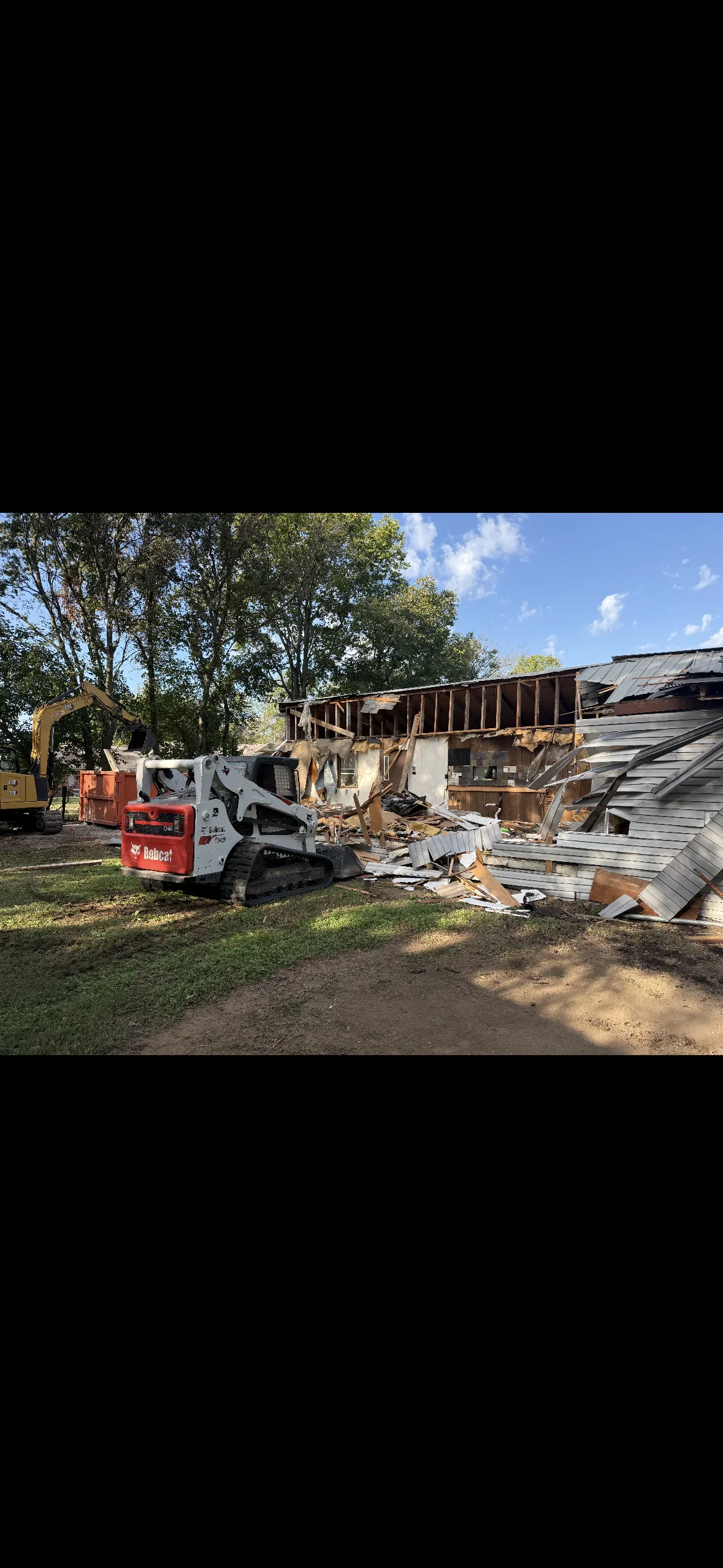 Bobcat skid-steer loader demolishing wooden commercial building with exposed framing and metal roofing