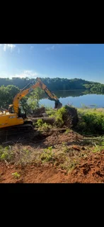 Yellow excavator on sloped terrain overlooking lake and mountains during site preparation